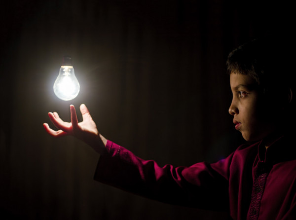An adolescent boy seems to be mentally lighting up an electric lamp.