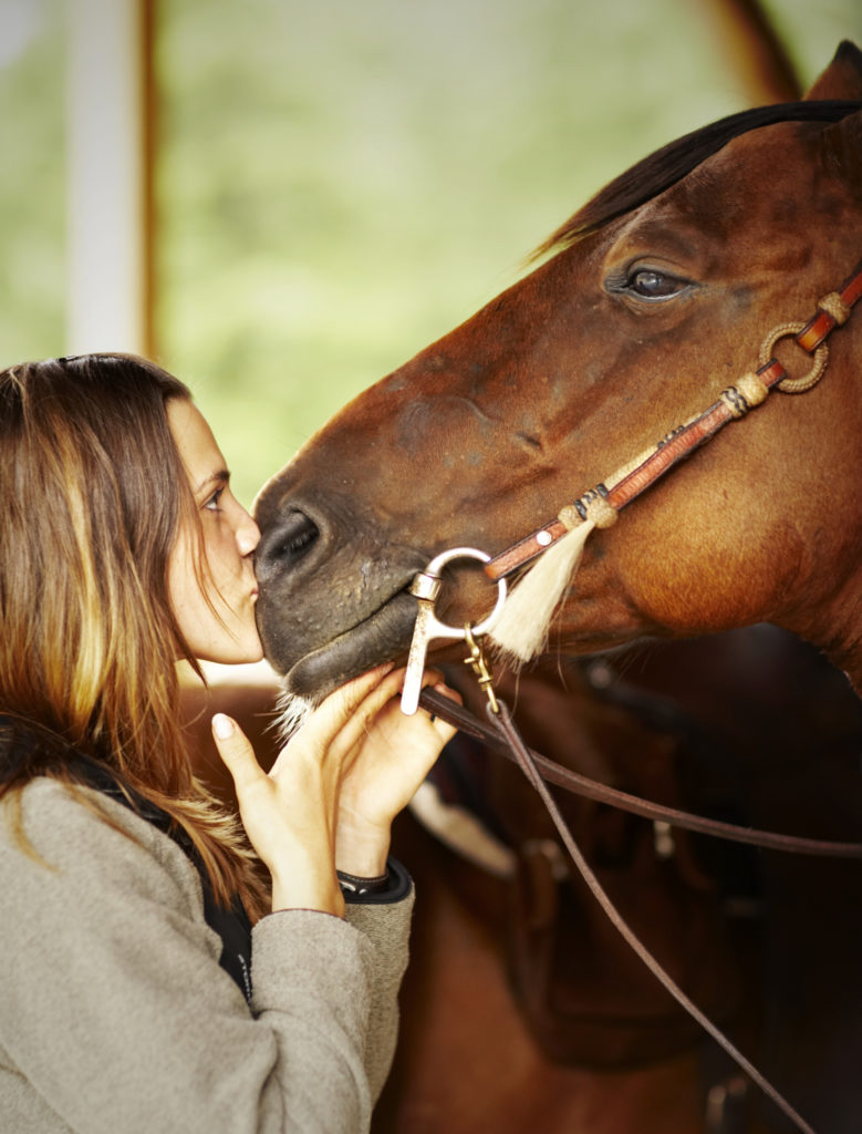 Woman kissing horse on nose.