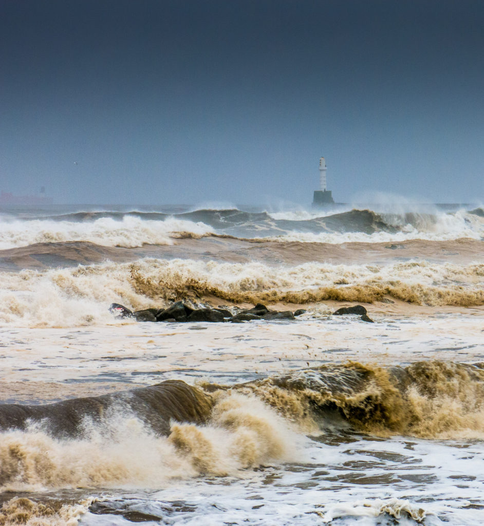 Extreme weather during Fall at Aberdeen beach, Scotland, UK, causes large waves to batter the shore. With Aberdeen lighthouse in the background against the North Sea. The sea looks aggressive and unforgiving.