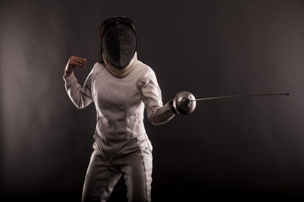 Portrait of woman wearing white fencing costume practicing with the sword.