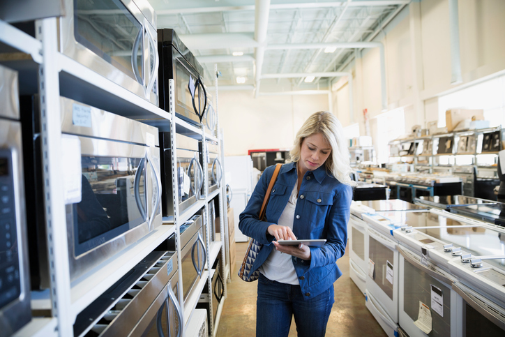 Woman with digital tablet shopping for microwave in appliance store