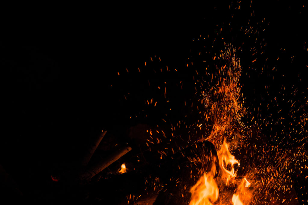 Sparks bounce off from a bonfire at night after a log thrown into it.