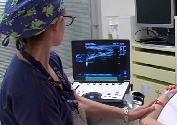  /><br />
<br />
<em>Dr Elizabeth Prentice uses ultrasound to guide a needle into the vein of a young CF patient.&nbsp;</em><br />
<br />
Prentice explains how this new ultrasound equipment—which is the size of a computer and is simply wheeled on its trolley around the hospital—has transformed practice for her and her colleagues. “We watch the screen and we can see that needle—the IV cannula—go directly into the vein,” she says. “We track it from the entry point in the skin, going down directly into the vein, watch it going through the vein wall and then follow the needle tip up the vein. It’s so precise, it’s like steering directly into the vein or the artery, whereas with the old probes, even two years ago, we would just vaguely see movement in the artery or vein.”<br />
<br />
Ultrasound scans are being used throughout RCH, from the wards to the operating theatre. “For a regular drip, we get a call from the ward saying, ‘We failed to get a drip in a child. The child is crying, the parents are distressed. Can you come and help?’ We take the ultrasound down and we scan the whole body of the patient and decide on the best vein,” says Prentice.<br />
<br />
Horror stories from the pre-ultrasound days are still in recent memory for doctors, she says: “With a chubby one-year-old, it was often difficult to get a drip in—people might have had five, six, seven attempts to get IV access. Now, we get the ultrasound, scan the baby and find the best vein. In the old days, it might have taken 30 minutes of delayed surgery and six or seven or eight attempts at IV access, Now after a few minutes and two or three attempts we get someone with the ultrasound.”<br />
<br />
The ability to scan even the smallest baby has all but ended the venous cutdown, an invasive procedure performed to access a child’s artery or vein. “With the old ultrasounds, we couldn’t get a good image and see the needle shallower than 1.5-2cm,” explains Prentice of the depth field of the probes, which didn’t really cater for tiny bodies. “The newer probes have made a huge difference because from 0 to 8mm of depth we can clearly see all the details, and clearly see the needle going right into the vessel. You set 0.5-0.8cm as your maximum depth, and you can see that tiny little vein or artery in the middle of your field, and instead of just seeing vague needle movement, you can see the tip of the needle go all the way into that 1 or 2 millimetre-diameter vein or artery.”<br />
<blockquote>Ten years ago, cystic fibrosis kids might have had big PICC lines in tiny veins, because doctors weren’t able to assess them with ultrasound.</blockquote><br />
For children who need a central venous catheter or PICC line inserted, as may occur with oncology or cystic fibrosis (CF) patients, ultrasound pre-scanning is standard says Prentice. “CF kids, who need lots of PICC lines, need their&nbsp;<a href=