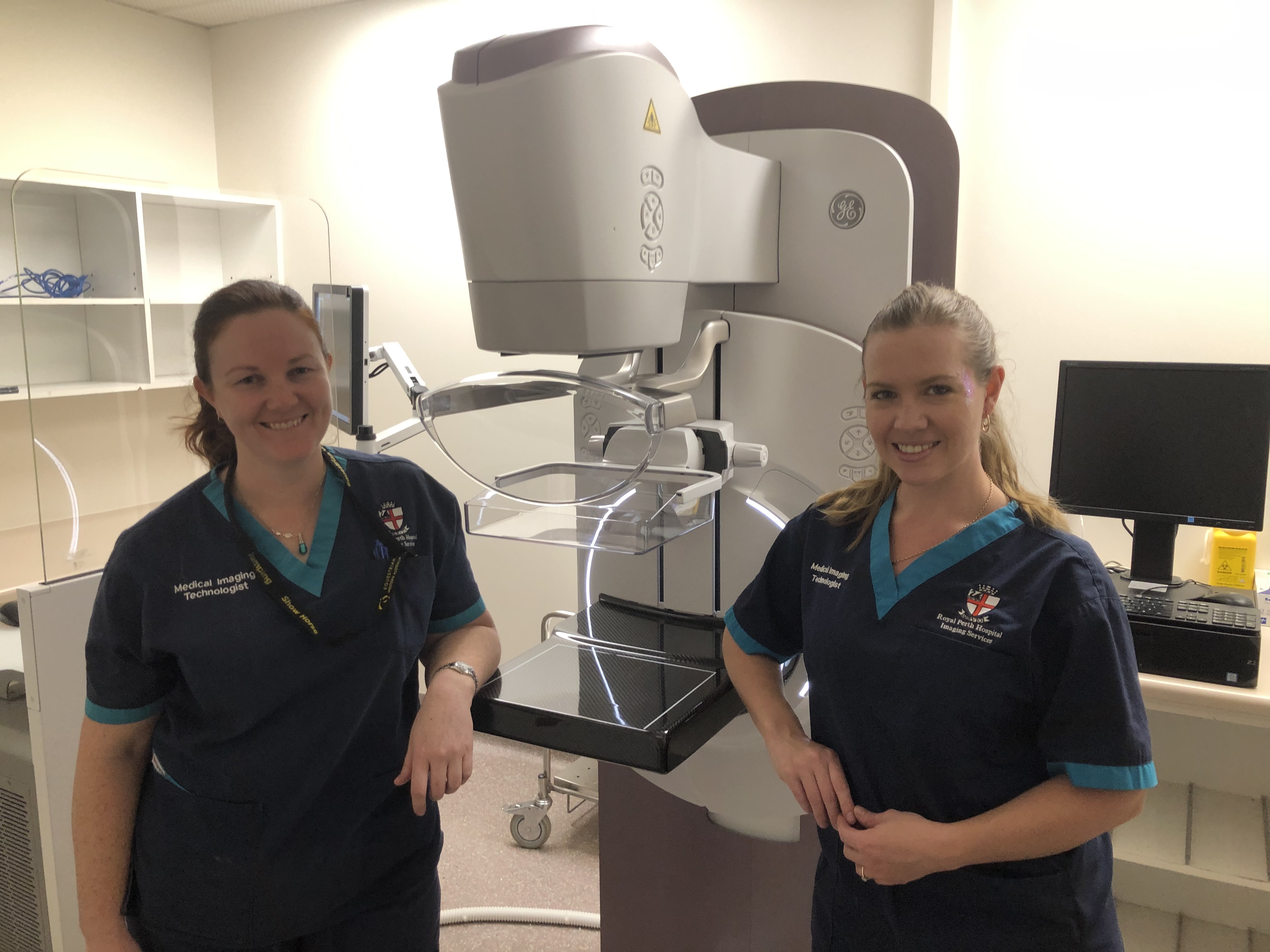 Two technicians stand in front of a Senographe Pristina mammography machine.
